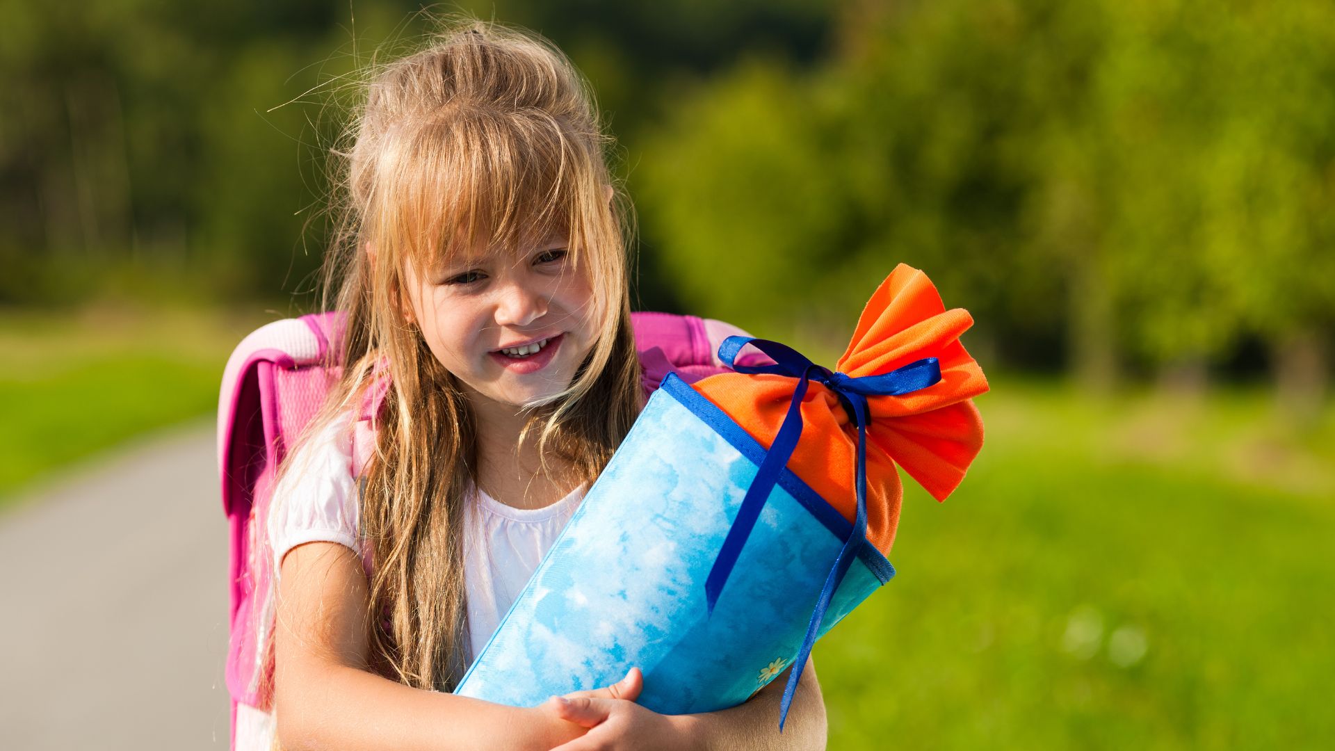 Kleines Mädchen Schulanfängerin Grundschülerin steht mit einer Zuckertüte vor einem grünen Naturhintergrund Schule
